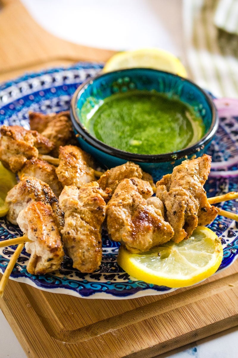 close up shot of malai boti skewers placed on a blue patterned plate with a slice of lemon.