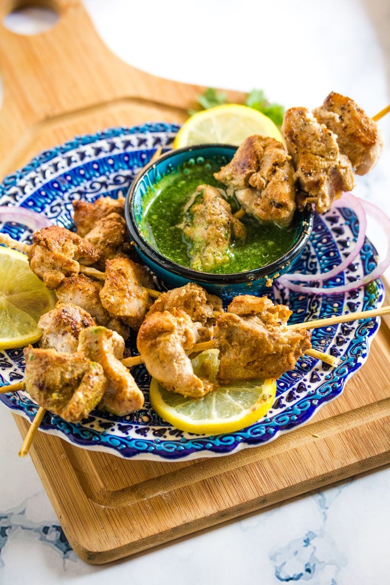 a skewer of grilled chicken pieces being dipped into a bowl of green coriander chutney.