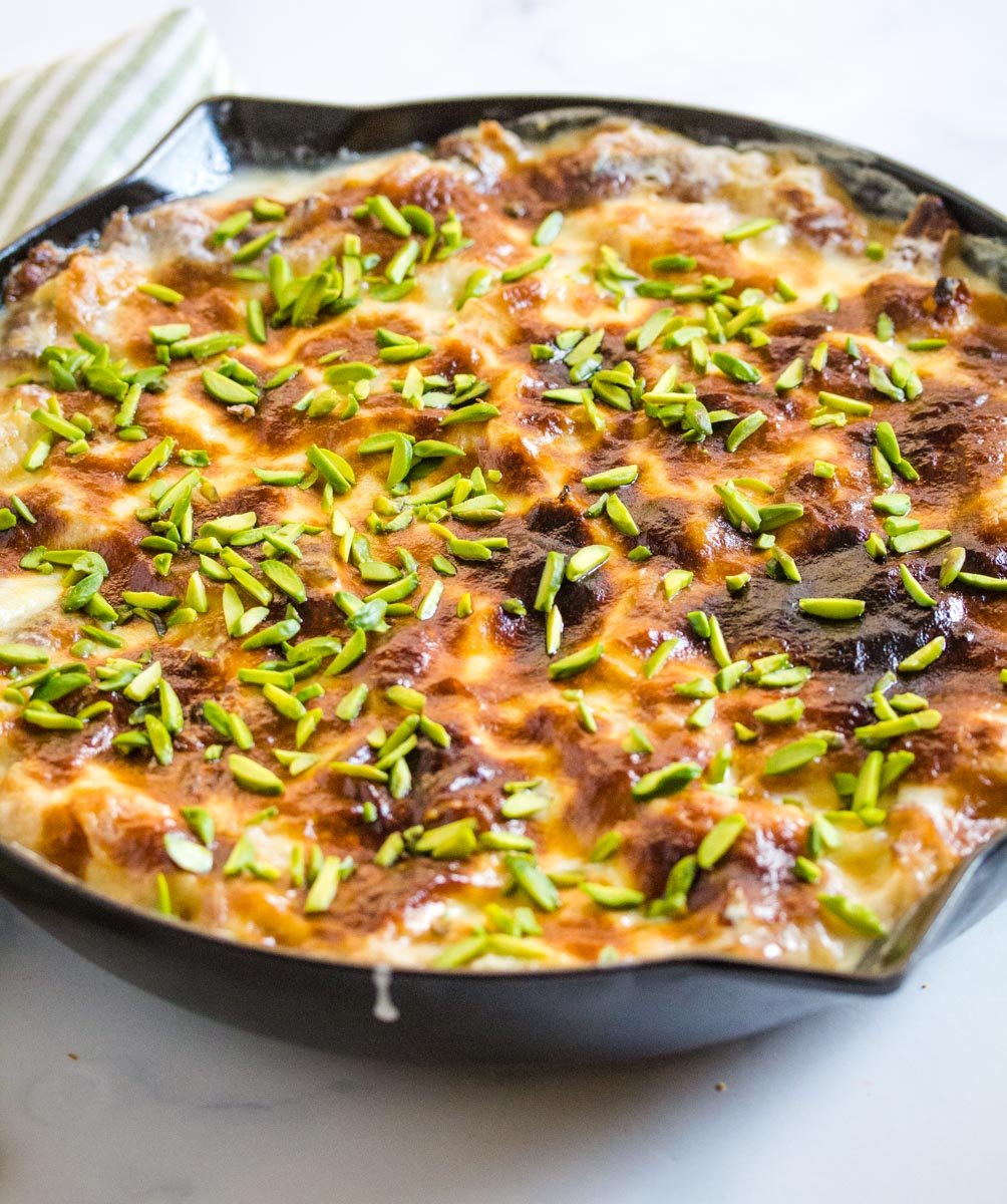 baked umm ali in a black cast iron skillet topped with pistachios.