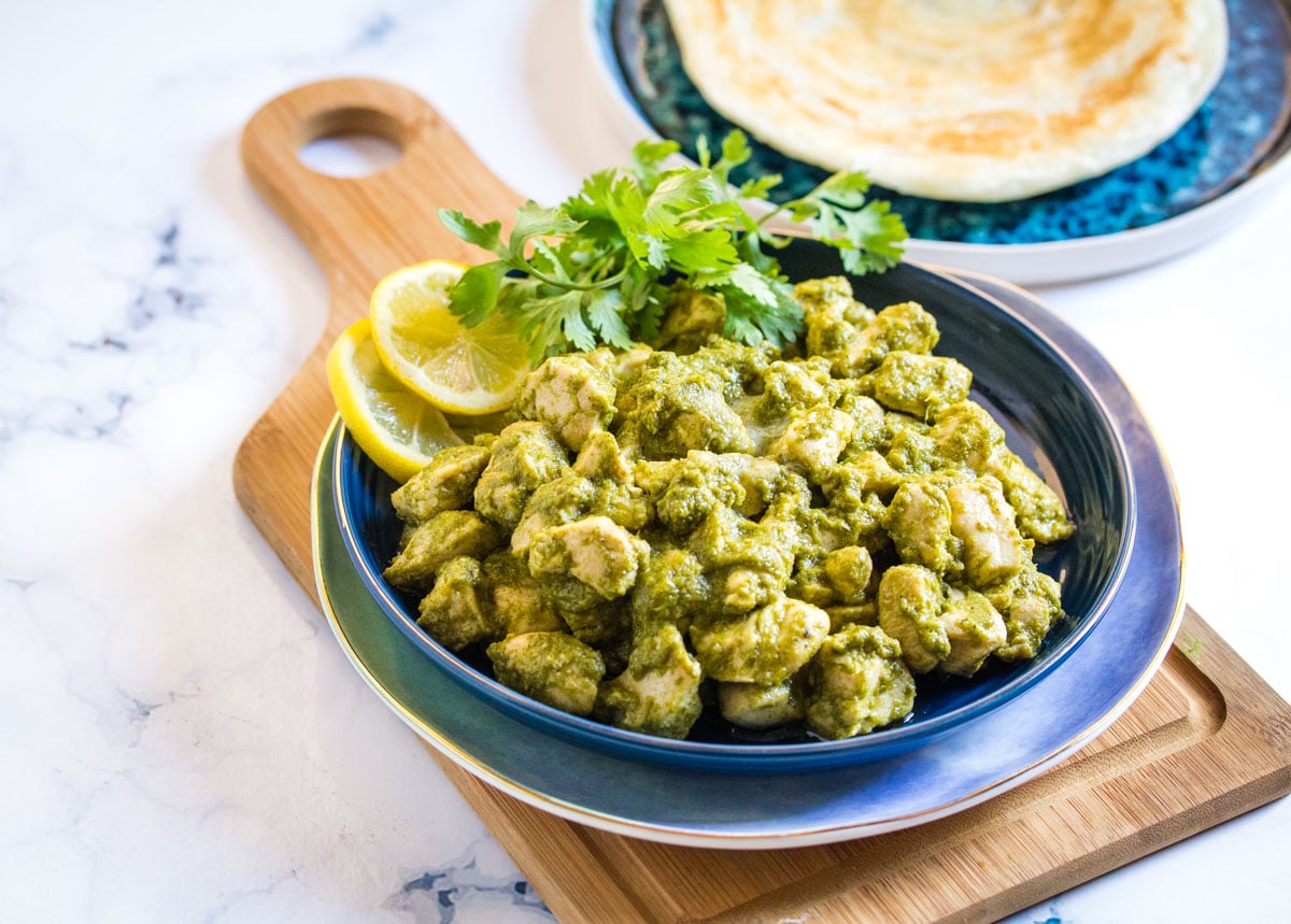 Green chicken curry served on a blue plate with a side of white paratha.