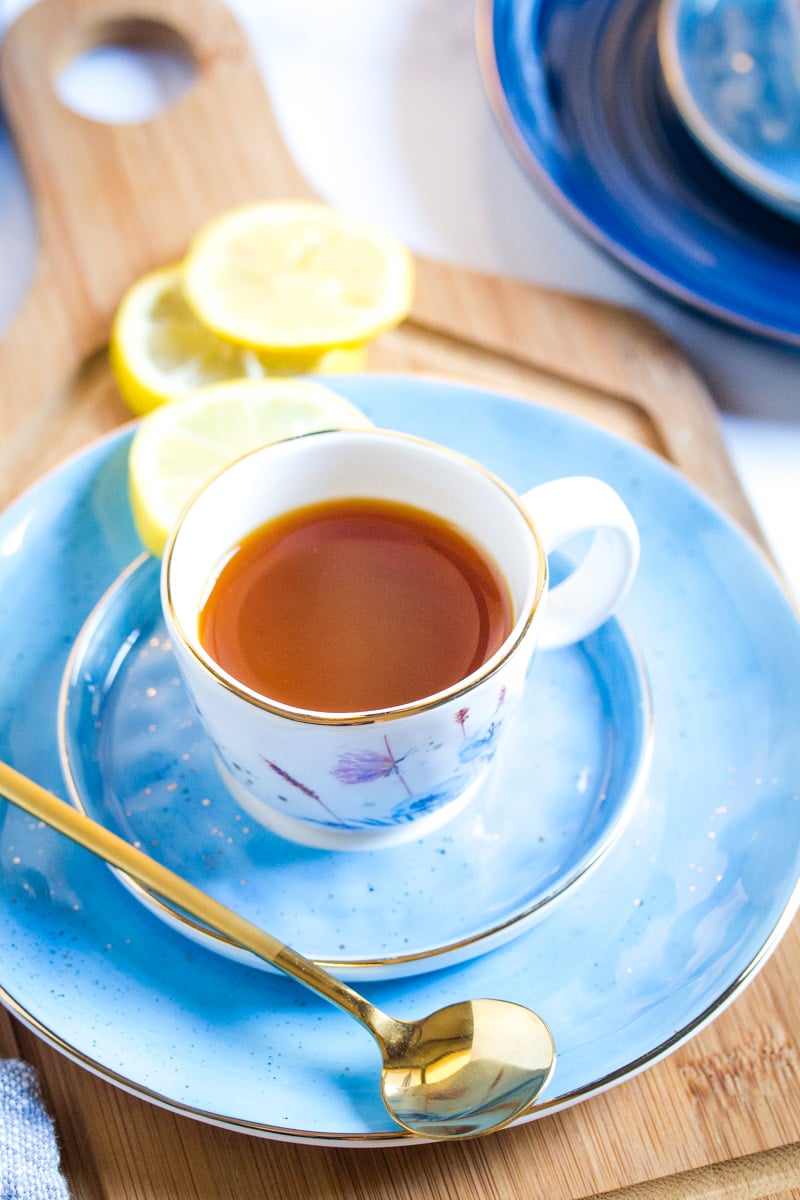 Lemon tea in a small white cup placed on a light blue plate served with lemon slices.