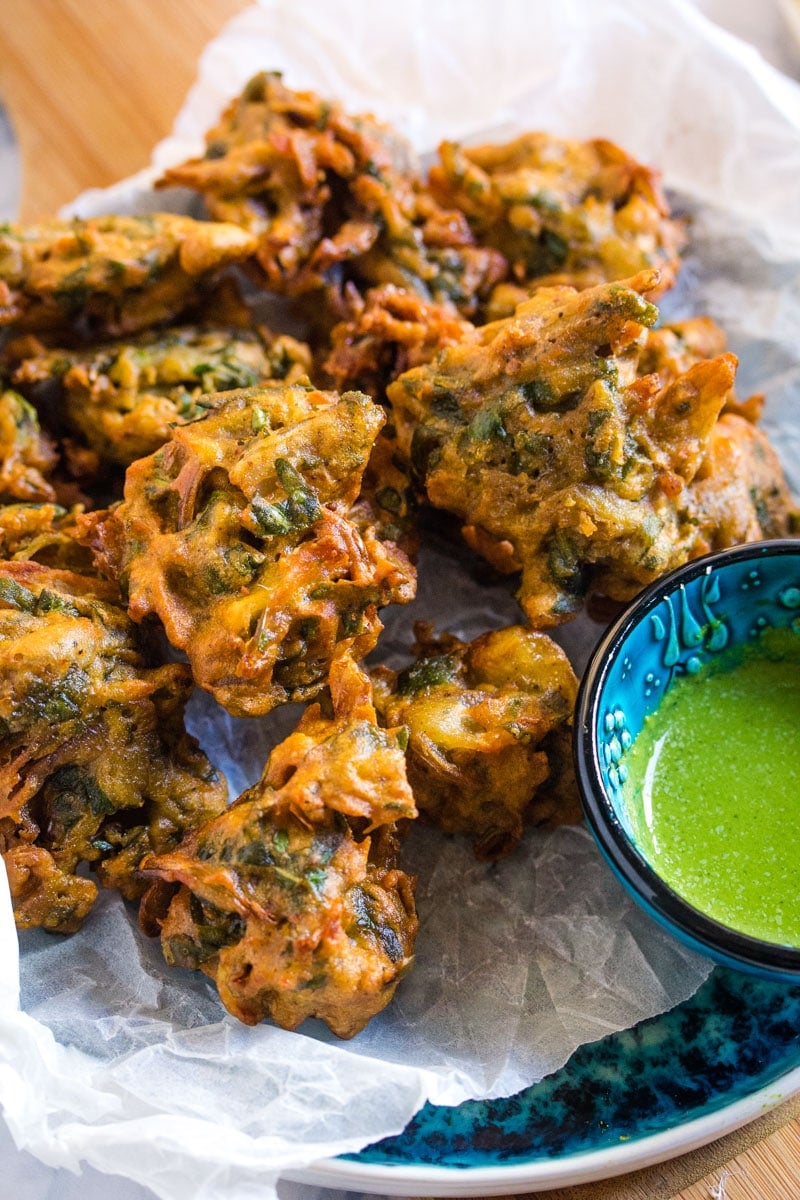 Close up shot of a pile of pakoras served with a small bowl of green chutney.