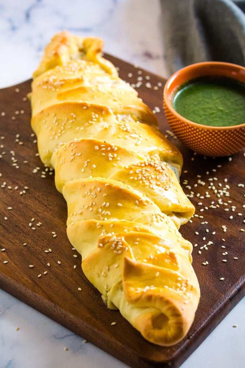 Stuffed bread with chicken filling on a wooden platter served with green chutney.