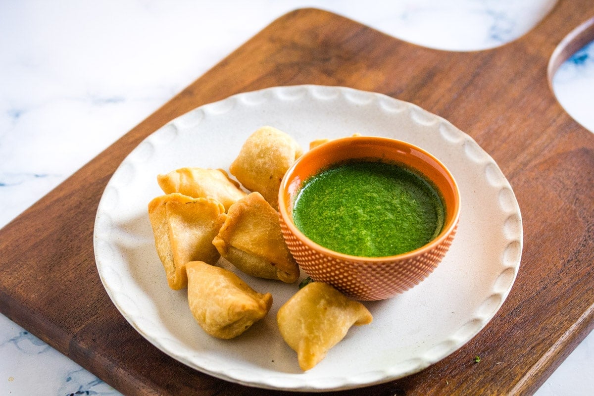 Green chutney served with mini samosas on a white plate.