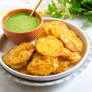 Pakistani aloo pakora on a light grey plate with green chutney.