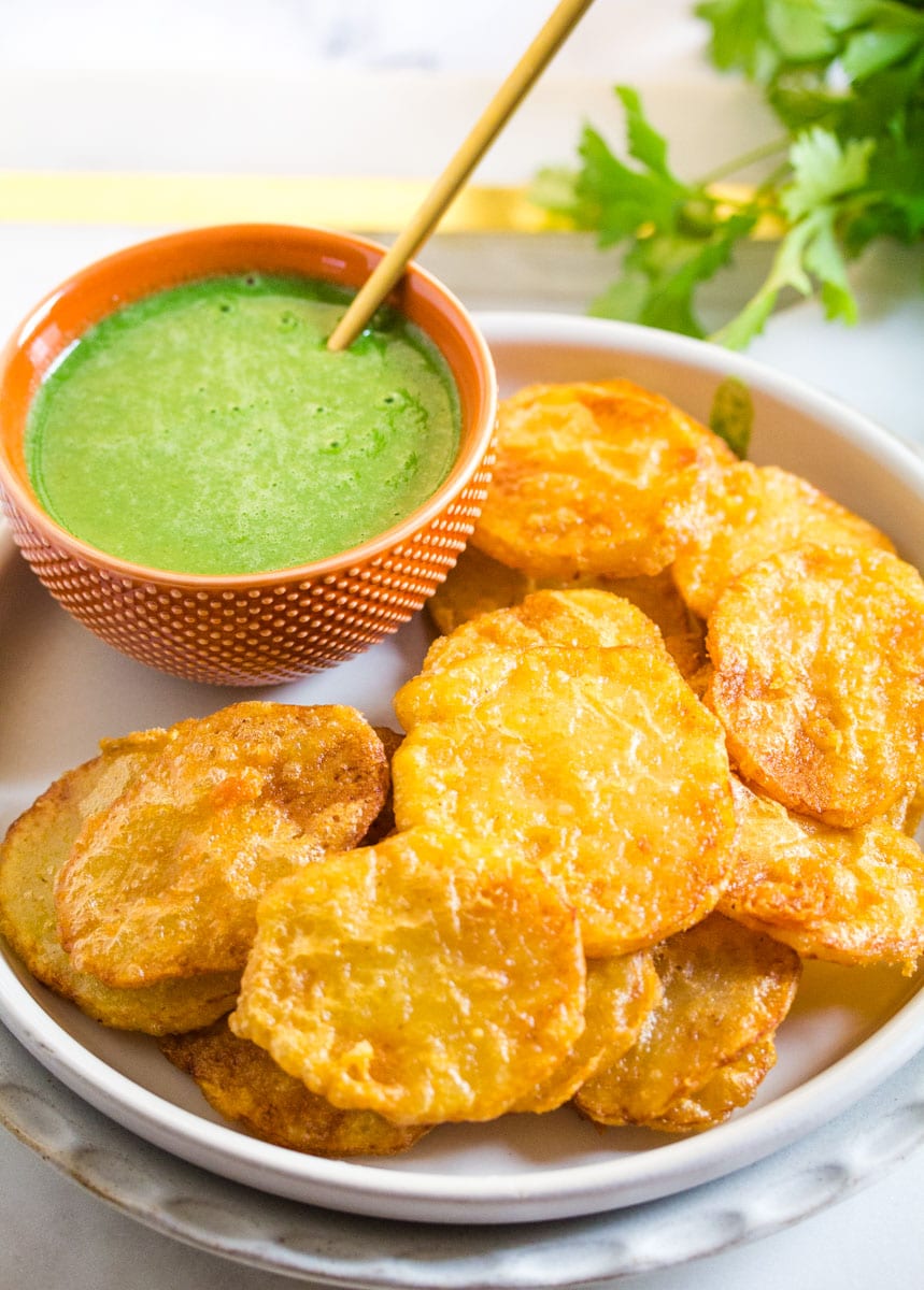 A plate of aloo pakora served with a bowl of green chutney.