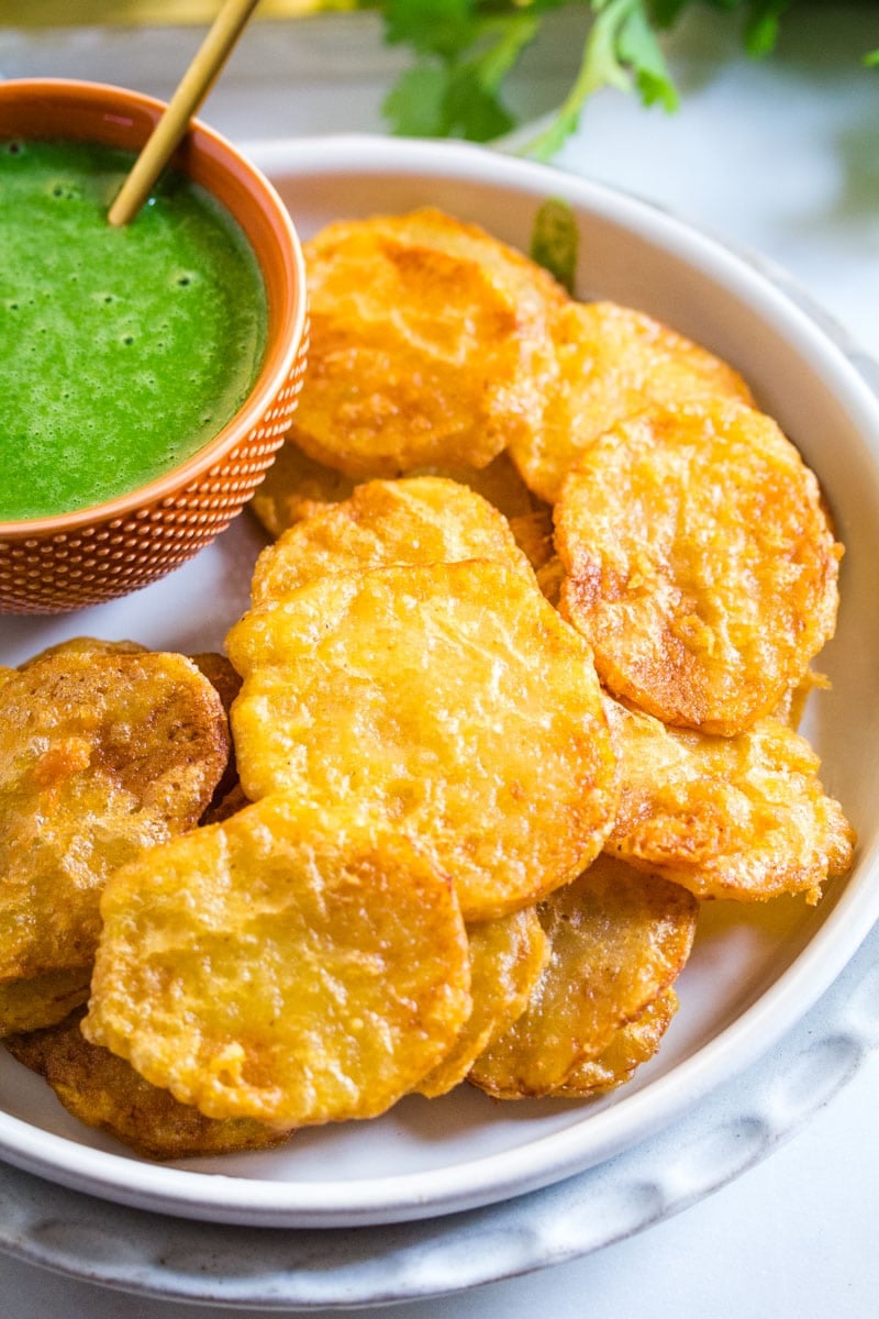 Close up shot of potato fritters with a side of green chutney.