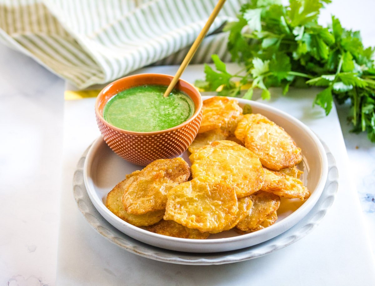 Pakistani aloo pakora on a grey plate with a side of green chutney.