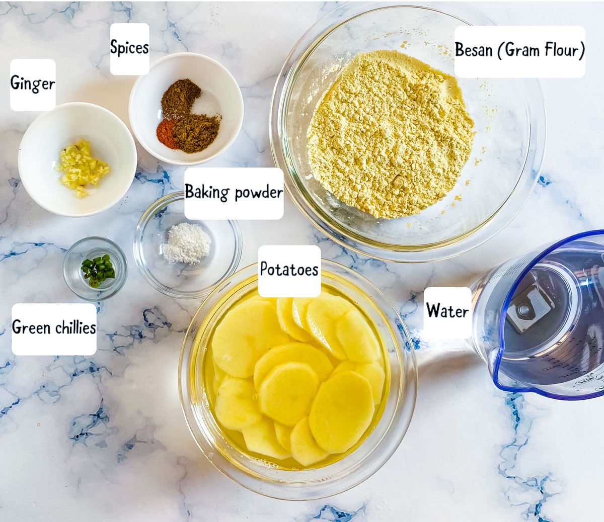 Ingredients for aloo pakora laid out on a white marble backdrop.