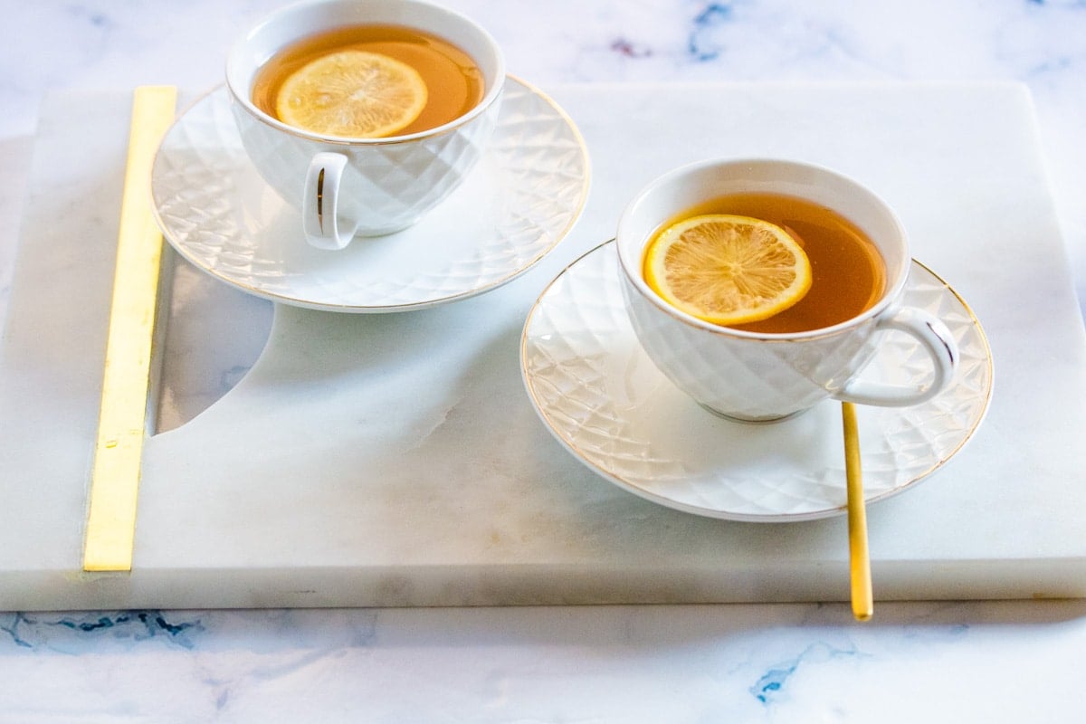 Two white cups of green tea on a marble slab.