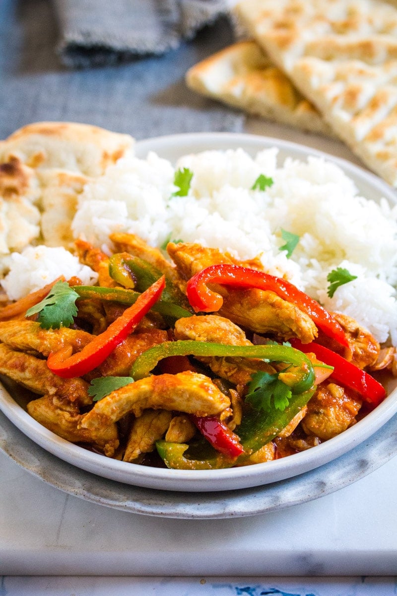 A serving of Jalfrezi with white rice and naan on a light grey plate..