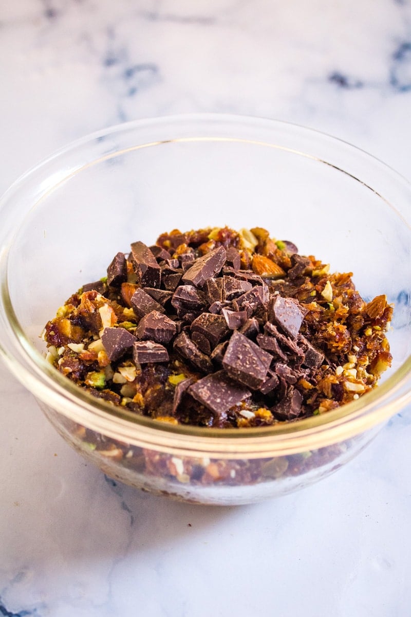 A mix of cooked dates, roasted nuts, and chopped dark chocolate in a mixing bowl.