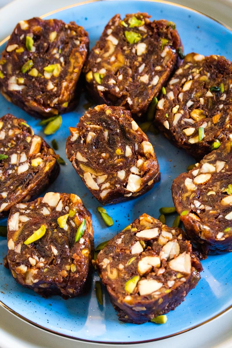 A close up shot of date roll made with assorted nuts on a blue plate.