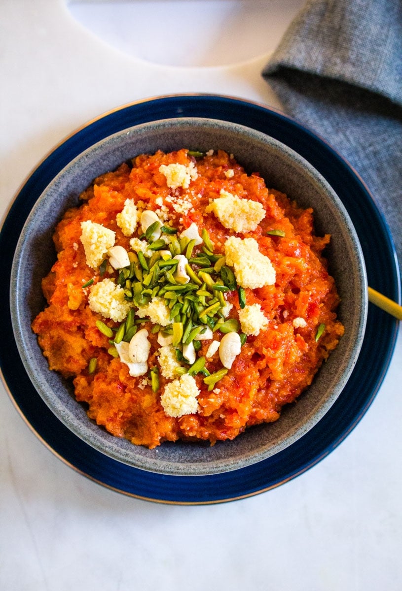 Overhead view of a bowl of carrot halwa placed on a white marble slab.