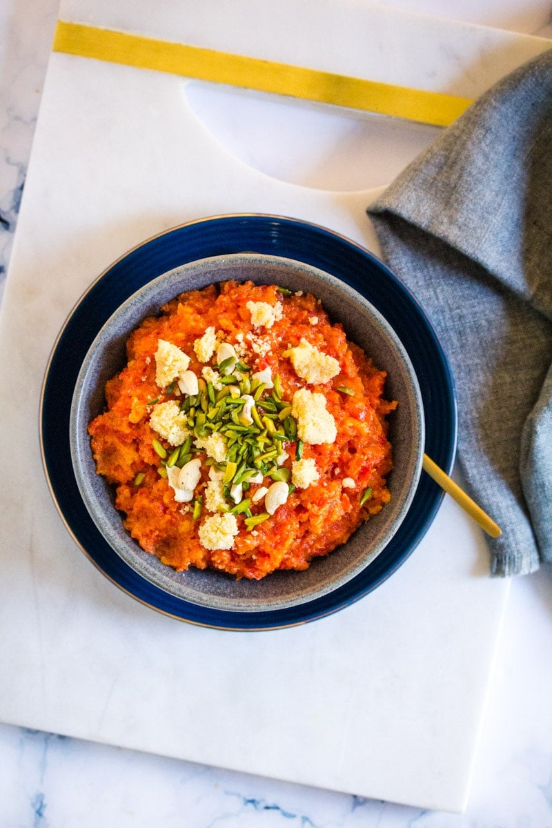 Overhead shot of gajar halwa topped with khoya and slivered pistachios.