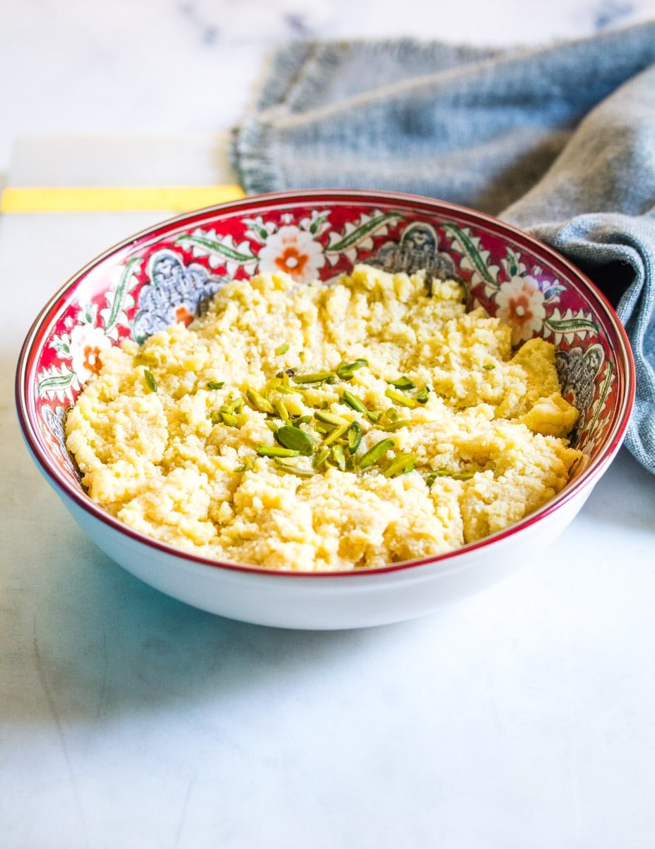 A bowl of khoya topped with slivered pistachios placed on a white marble slab.