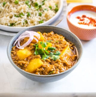 Aloo Keema served in a grey bowl and topped with coriander and sliced onions.