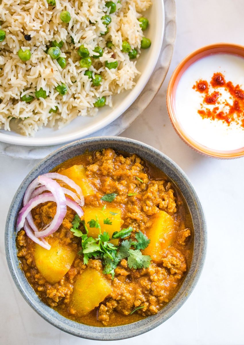 Overhead shot of aloo keema served with matar pulao and yogurt. 