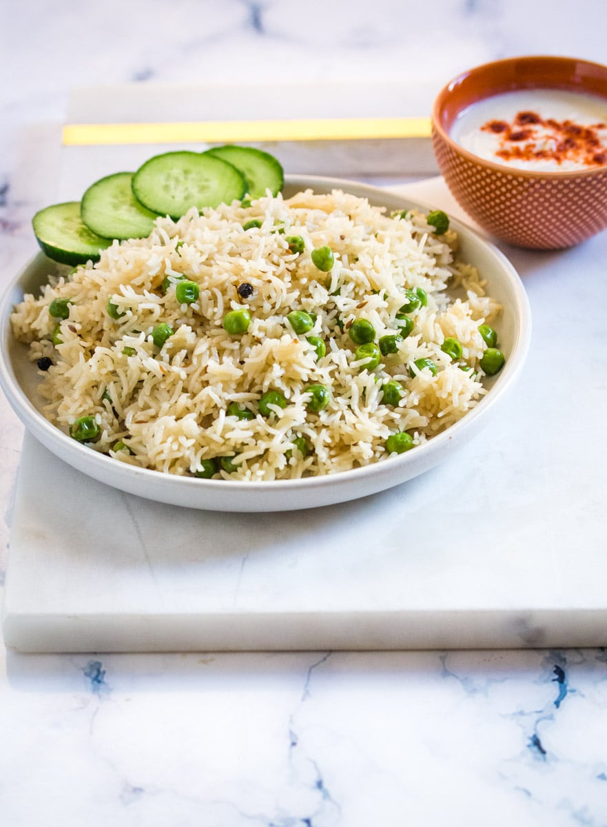 A plate of peas pulao served with yogurt and cucumber.