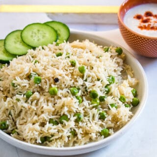 Matar pulao served with sliced cucumbers and a bowl of yogurt raita.