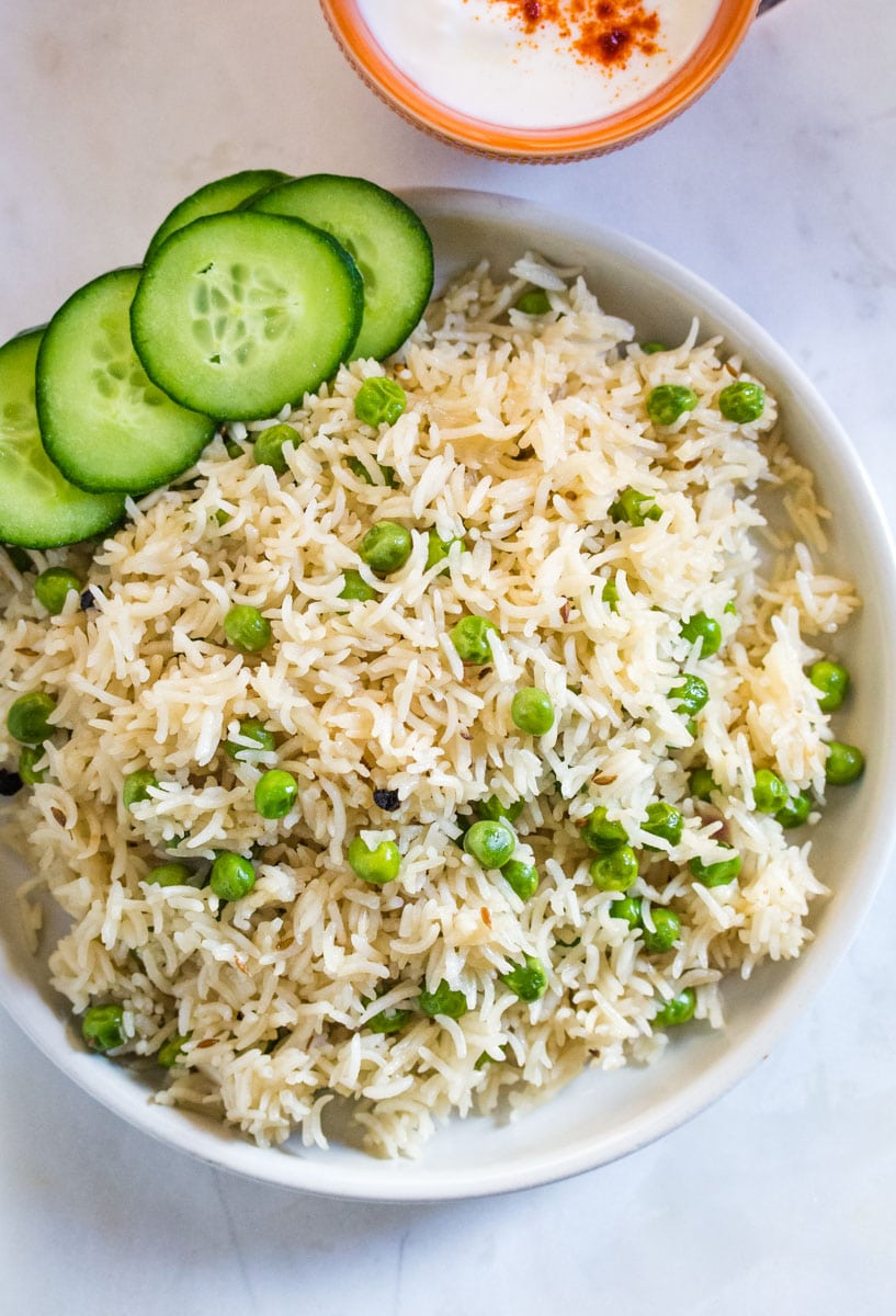 Overhead shot of matar pulao served in a white plate with cucumber slices.