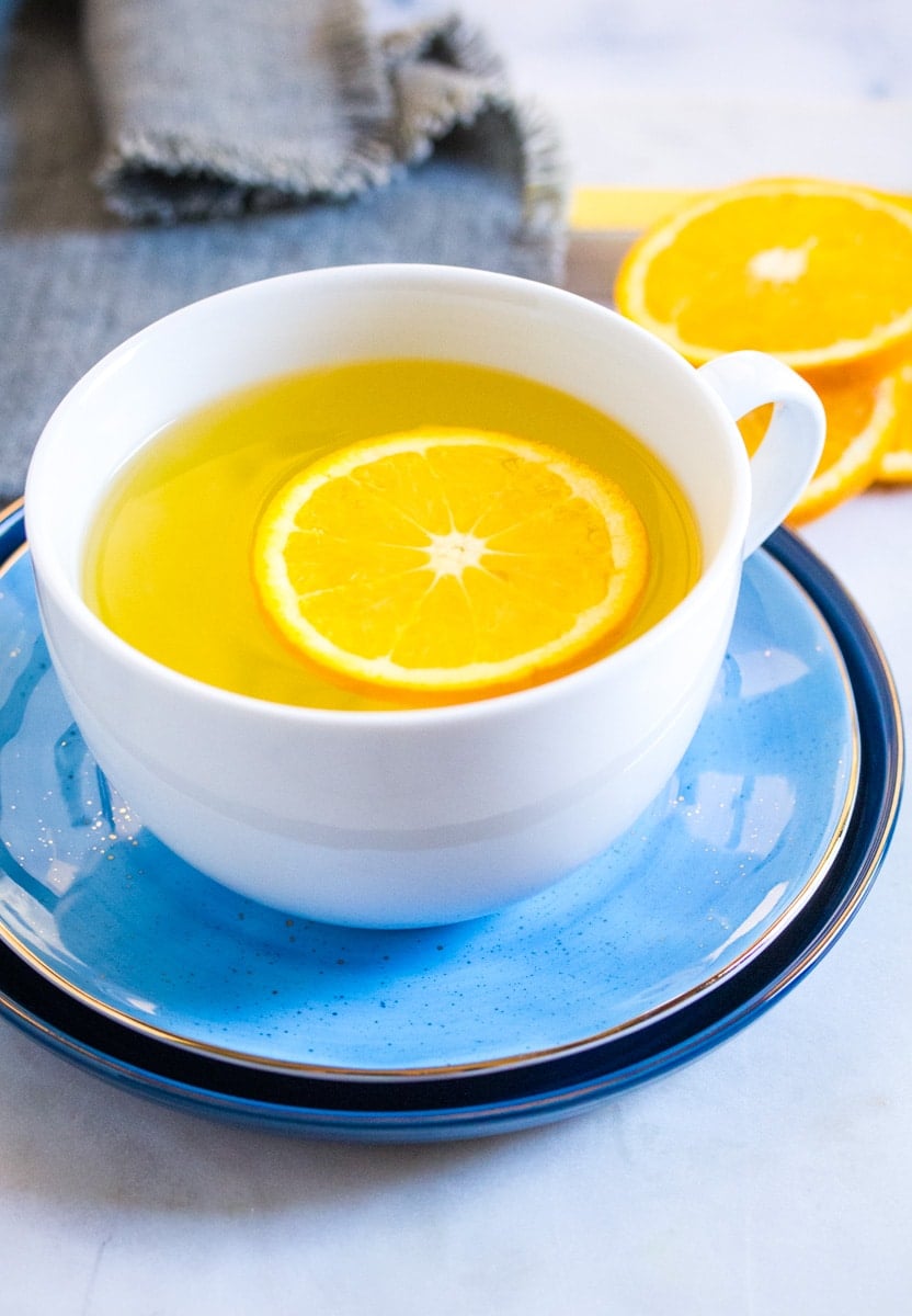 A white mug of orange tea served with a slice of fresh orange.