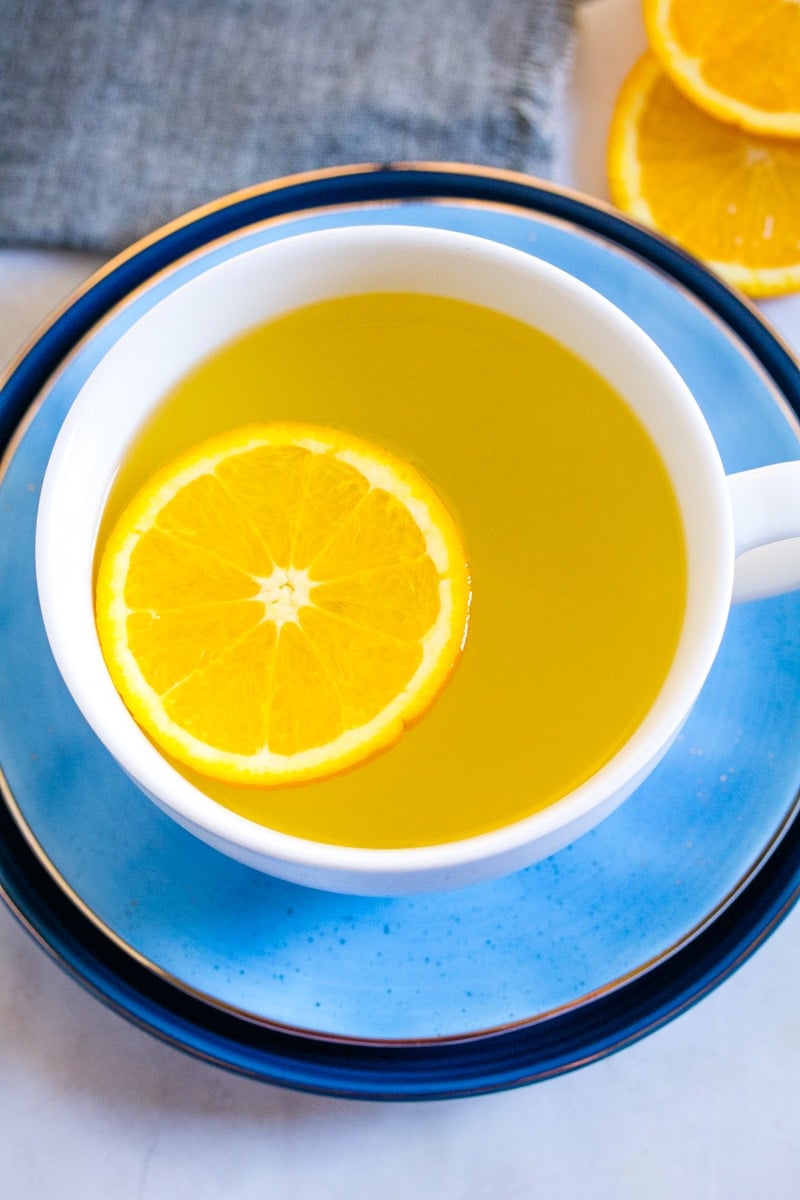 Overhead shot of orange tea in a large white mug topped with an orange slice.