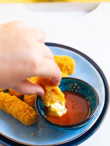 Dipping Crispy Doritos Mozzarella sticks on a sauce on a blue plate.