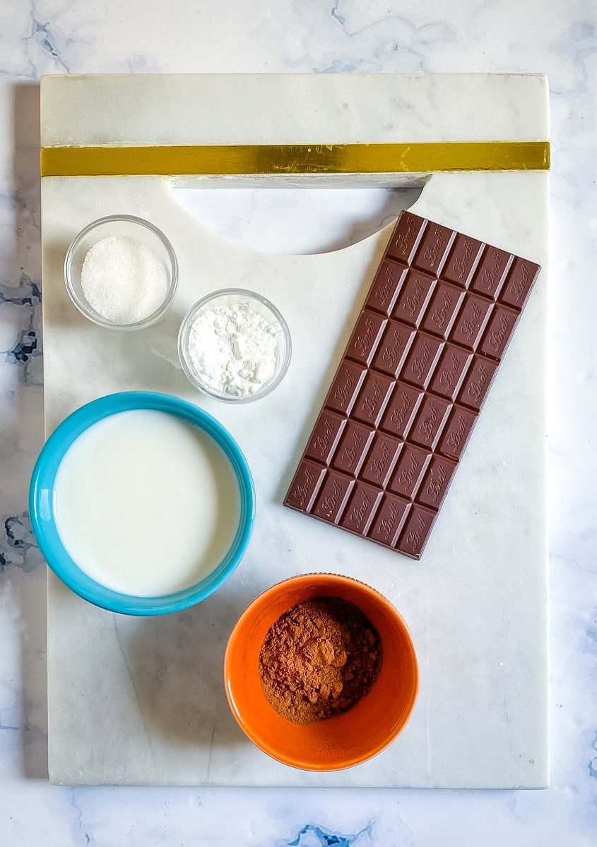 Italian hot chocolate ingredients in bowls: milk, sugar, cornstarch, cocoa powder, and chocolate bar.