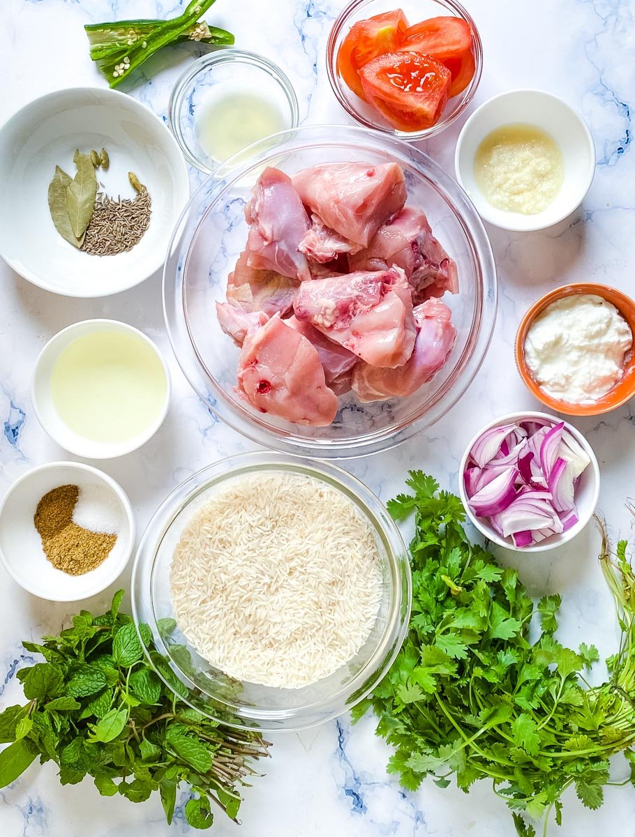 Ingredients needed to make chicken pulao laid out on a white backdrop