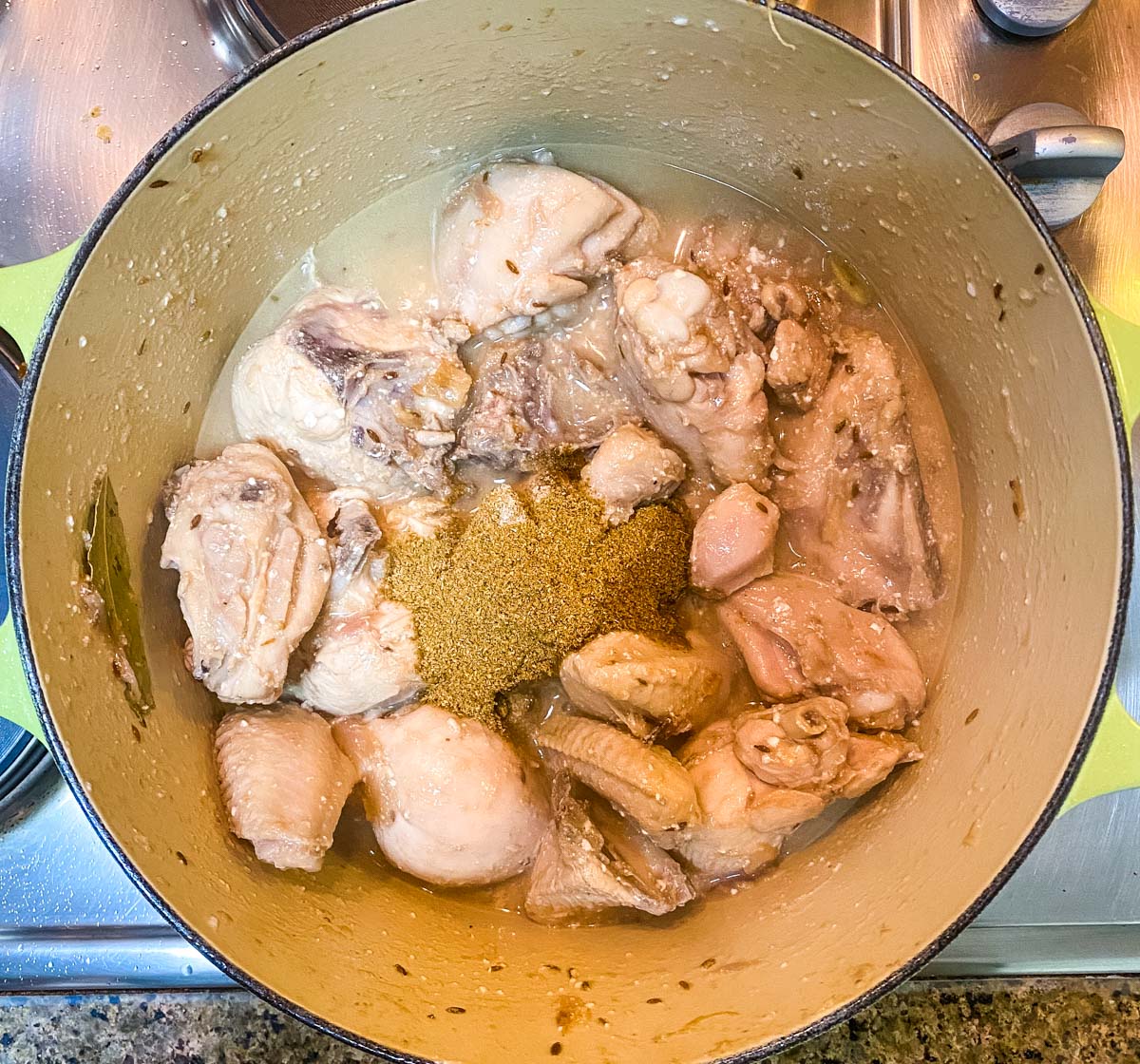 Powdered spices added to cooked chicken in a pot.