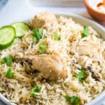 Chicken Pulao served on a light grey plate with a side of yogurt in a small orange bowl.