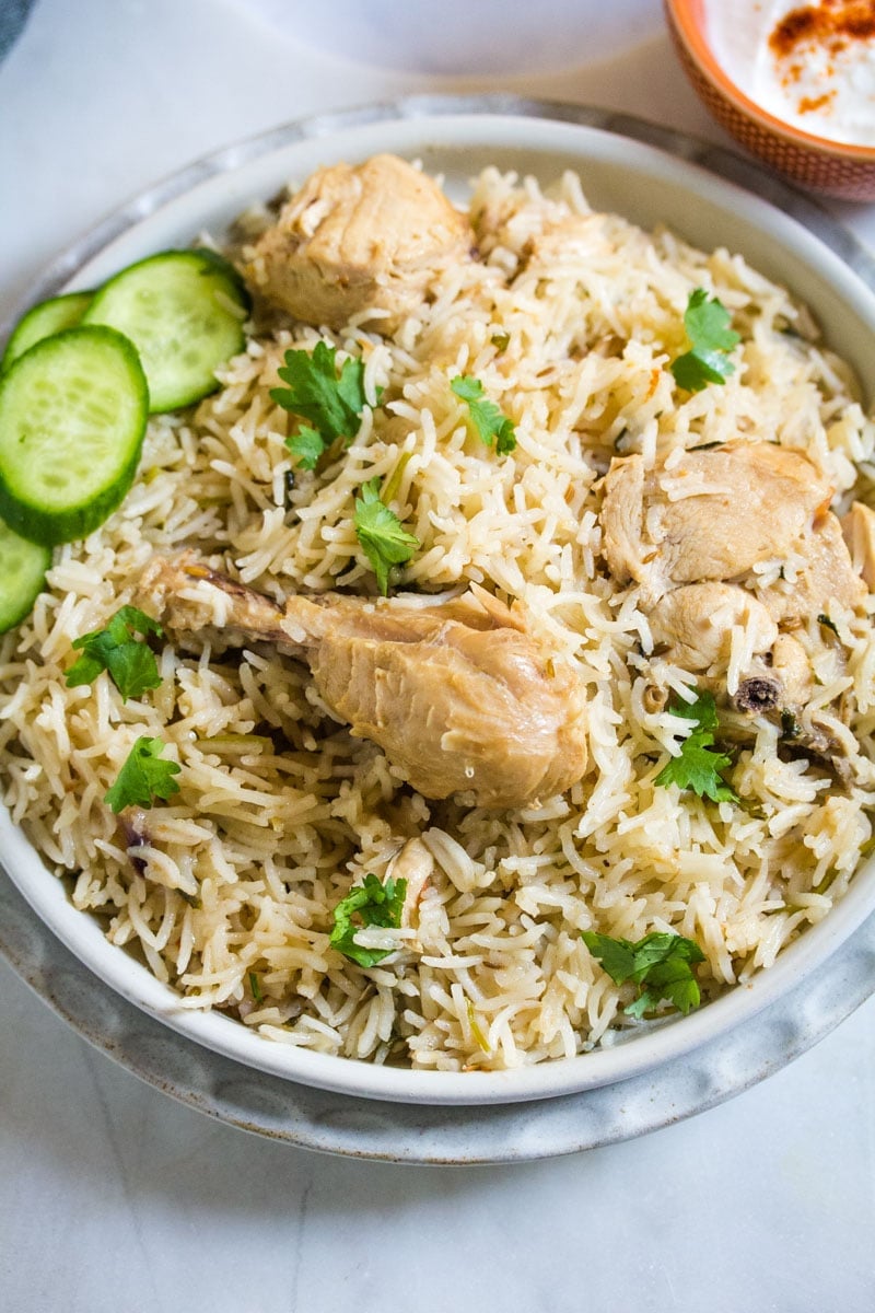 An overhead shot of chicken pilao topped with chopped coriander and slices of cucumber.