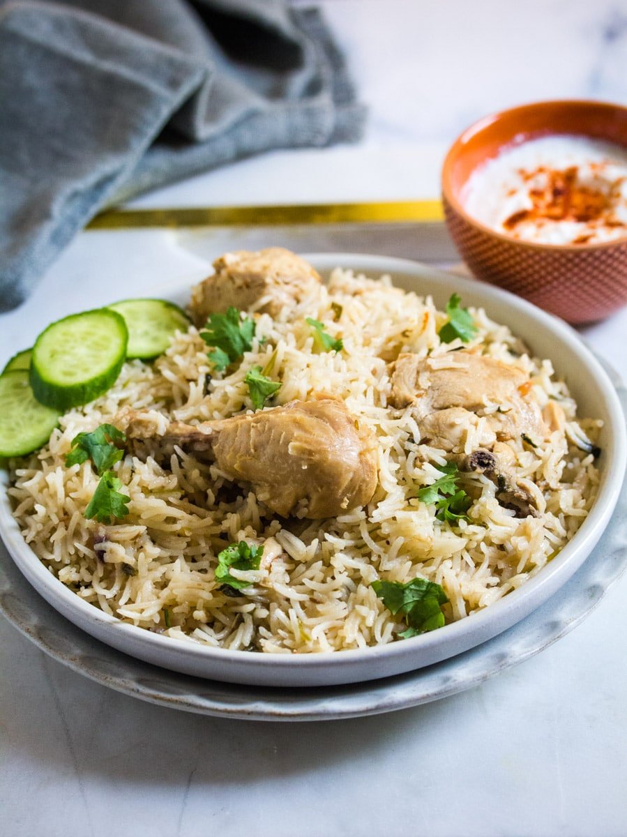 A plate of chicken pulao topped with chopped cilantro and cucumber slices on a grey plate.
