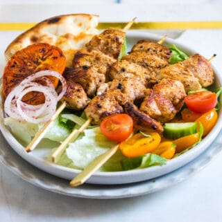 Chicken Sheesh Tawook served on a white plate with naan bread and salad.