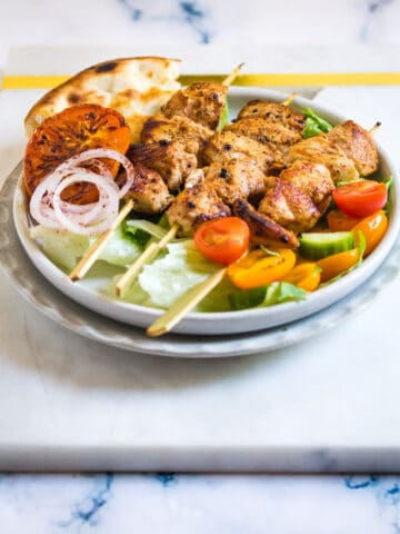 Chicken sheesh tawook on a bed of green lettuce with a side of salad.