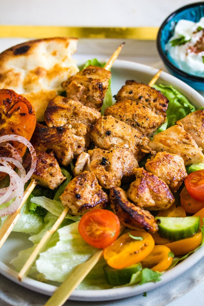 Close up shot of shish taouk served with naan, sumac onions, and grilled tomatoes.