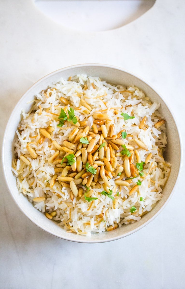 Lebanese rice served in a white bowl, topped with pine nuts and chopped coriander. 