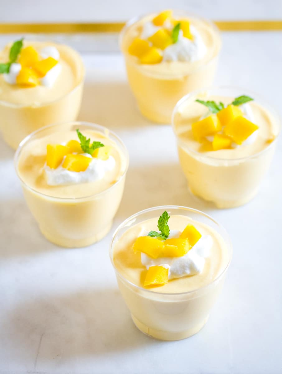 Mango mousse served in small plastic cups topped with whipped cream and fresh mango.