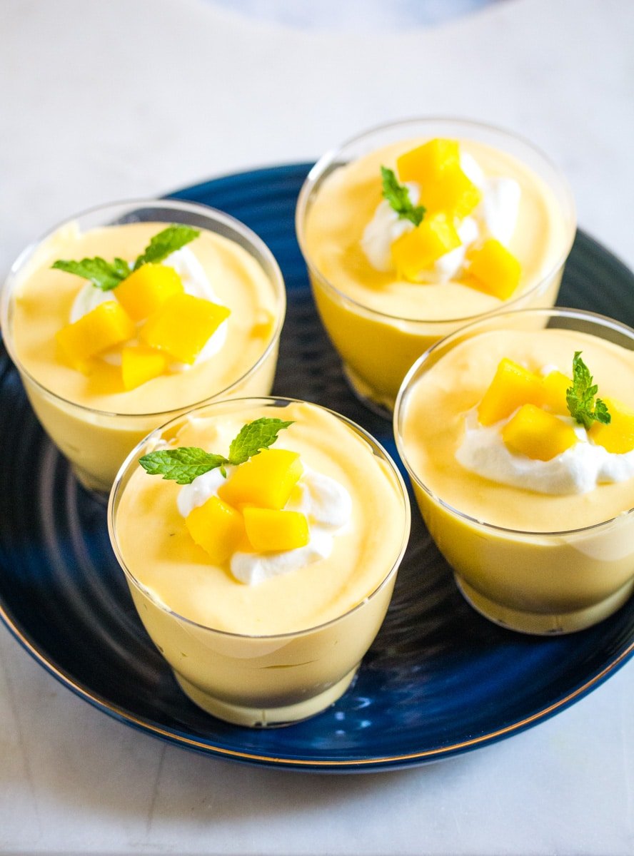 Four clear cups filled with mango mousse on a blue plate. 