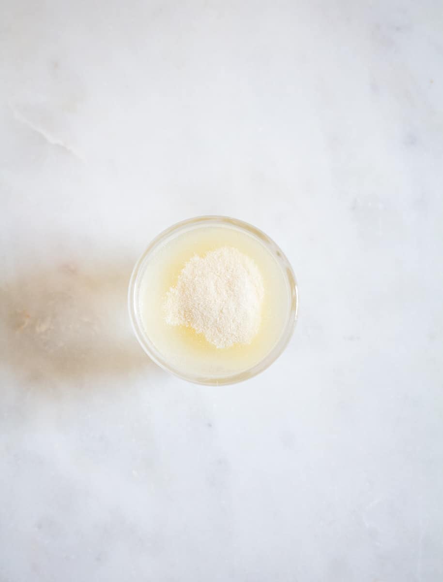 Gelatine powder mixed with water in a small bowl on white marble background.