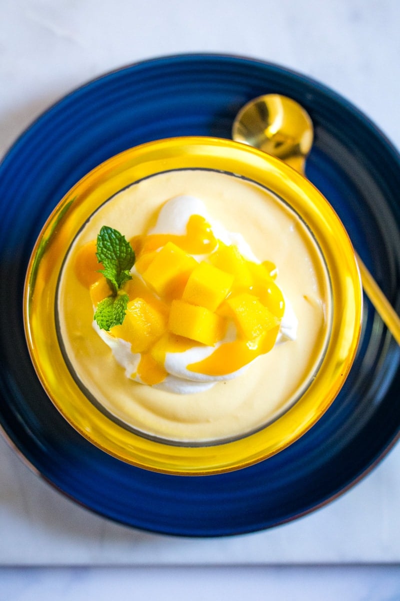 Overhead shot of mango mousse topped with cubed mangoes and mint leaves.