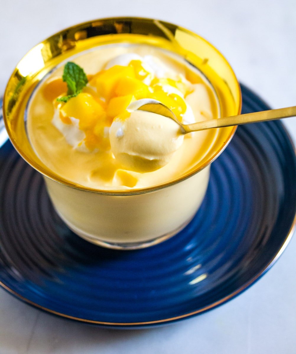 A spoonful of mango mousse being scooped out of a bowl on a blue saucer.