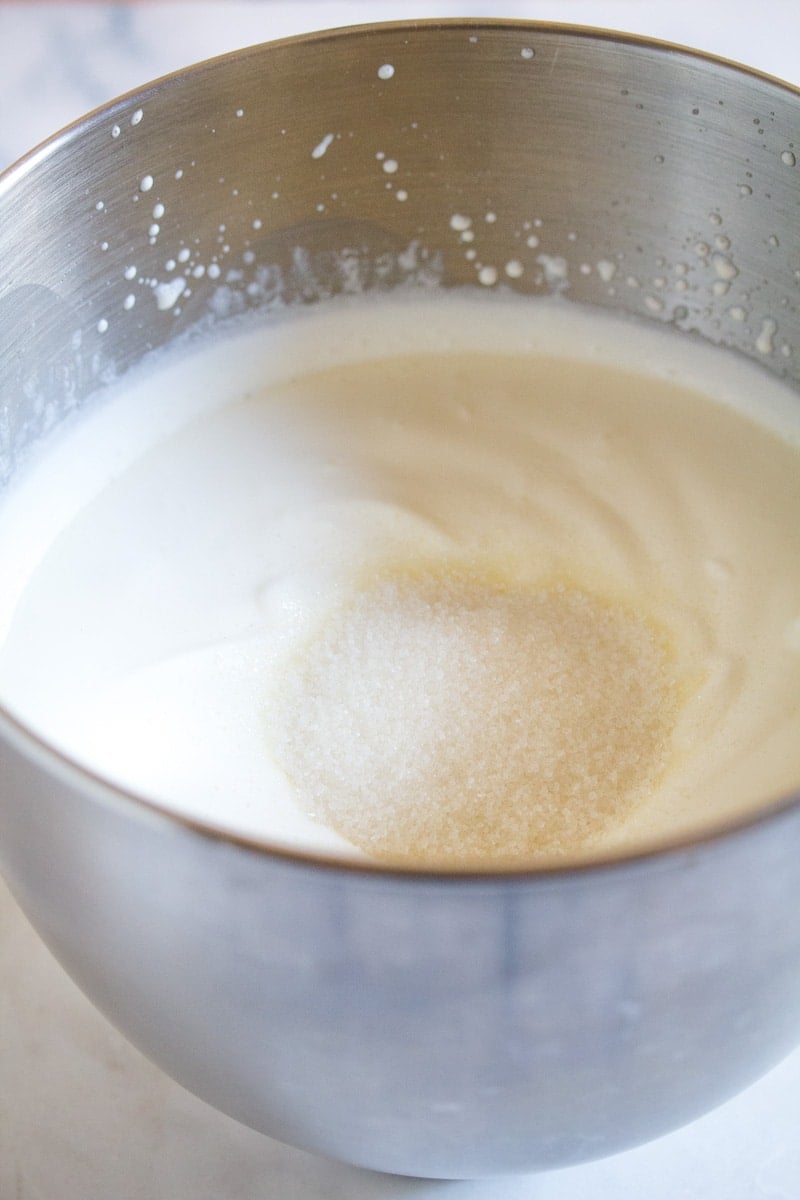 Granulated sugar combined with whipped cream in a metal bowl.