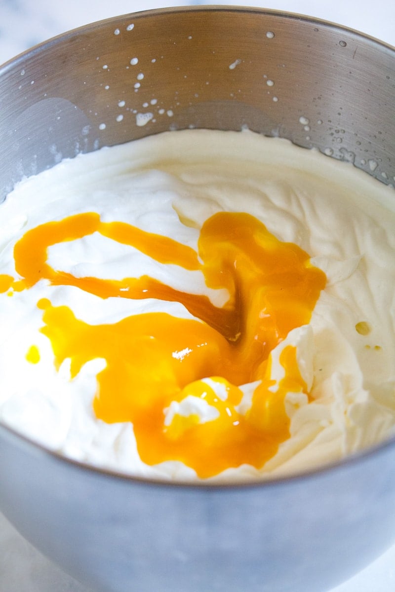 Mango pulp in whipped heavy cream in a metal mixing bowl.