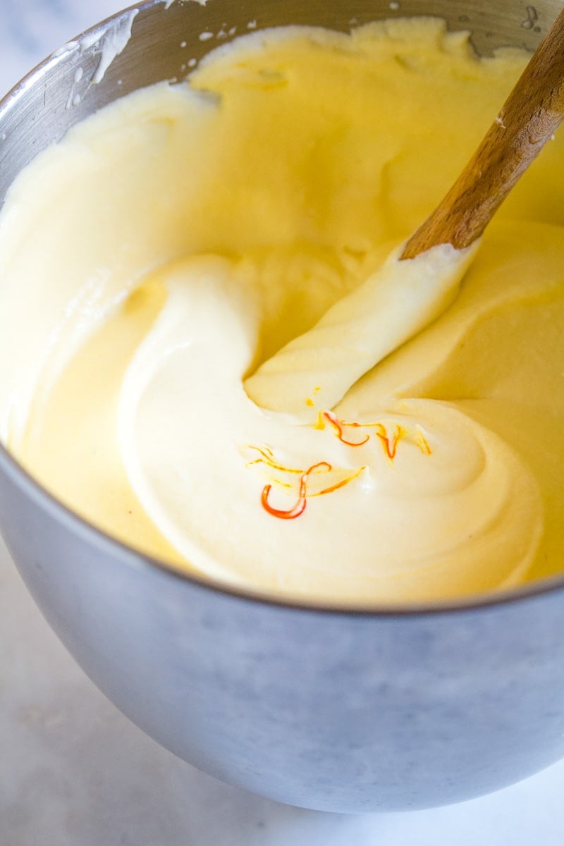 Few drops of yellow food color in mango mousse in a steel bowl.