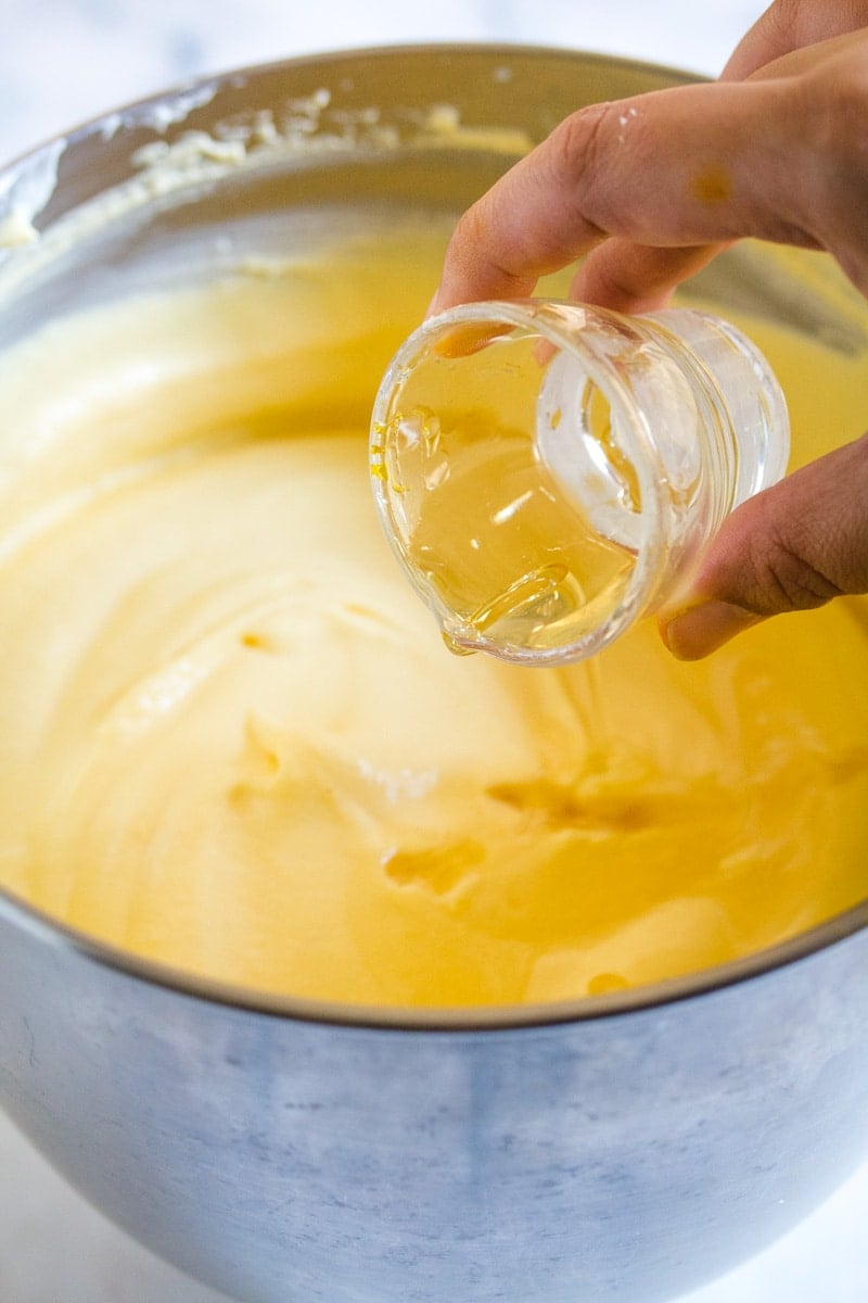 A shot of gelatine dissolved in water being poured into a mixture of mango pulp and whipped cream.