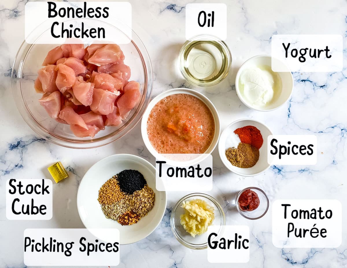 Ingredients for achari chicken laid out on a white marble backdrop.