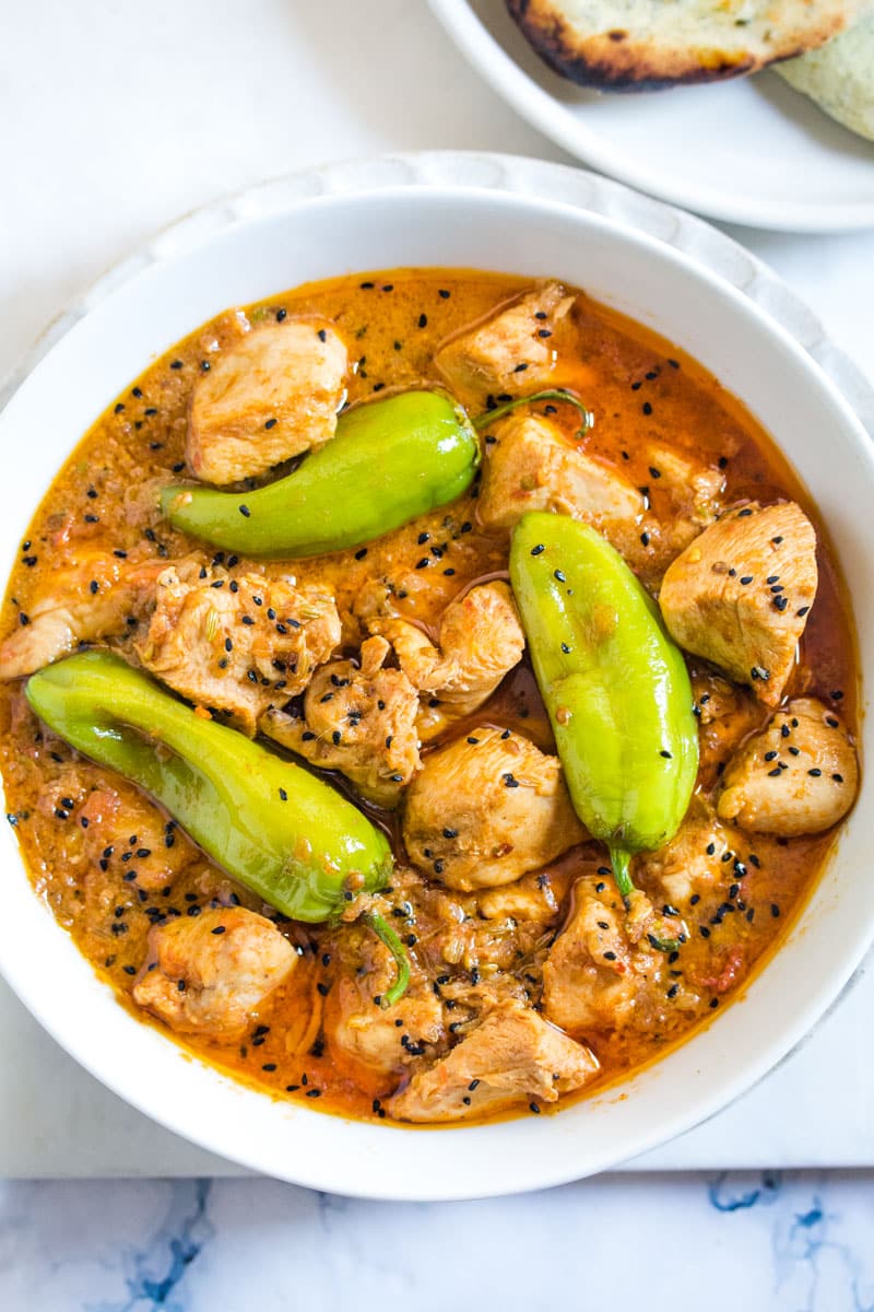 Overhead shot of chicken achar in a white bowl and topped with stuffed green chilies.