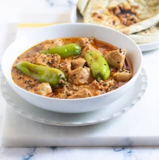 Pakistani Achari Chicken served in a white bowl, topped with stuffed chilies, and a side of naan.